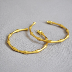 Macro shot of gold-plated bamboo joint hoop earrings on textured grey fabric