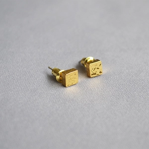 Macro detail of geometric gold-plated stud earrings with irregular hammered texture surface