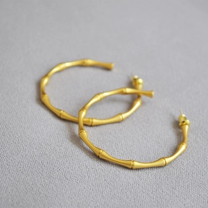 Macro detail of gold bamboo-shaped hoop earrings with a matte metallic texture