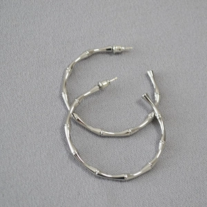 Macro shot of silver bamboo-textured large hoop earrings on a grey textured fabric background