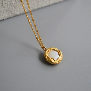 Détail d'un pendentif en perle baroque avec bordure dorée ondulée sur chaîne à perles