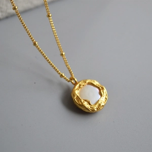 Collier doré vintage français avec pendentif perle baroque sur fond texturé foncé