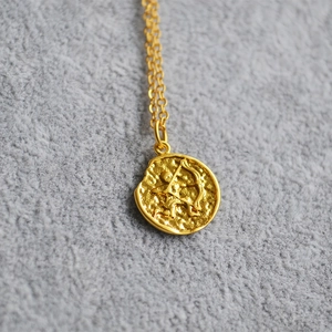 Macro shot of gold coin necklace with Sagittarius zodiac relief on a textured pendant