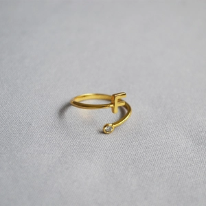 Macro shot of gold adjustable ring featuring letter F and a round sparkling zircon stone