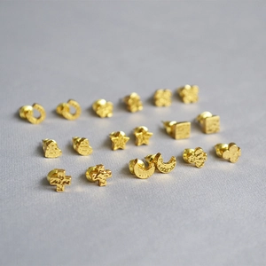 Macro detail of gold-plated stud earrings with handcrafted hammered texture on gray fabric