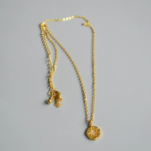 Detail of 18K gold-plated coin necklace featuring a zircon starburst pendant and adjustable chain
