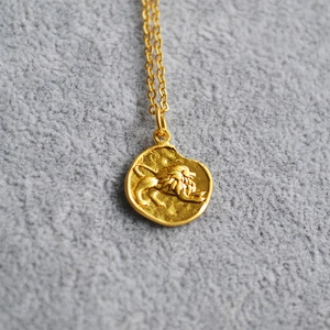 Macro shot of gold Leo zodiac relief pendant on a minimalist thin chain necklace
