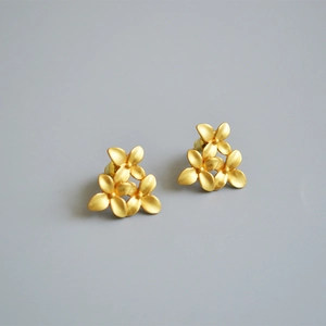Close-up of matte gold flower stud earrings with detailed three-petal floral texture