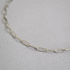 Macro shot of polished silver paperclip chain necklace on gray fabric texture
