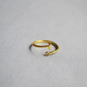 Close-up of golden T-shaped open ring with a single clear crystal on grey fabric
