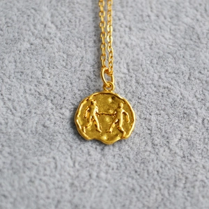 Macro detail of gold Gemini zodiac coin pendant necklace with embossed coin relief