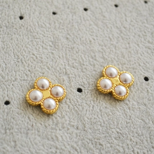 Gold plated brass four-leaf clover stud earrings with white pearls on grey fabric background