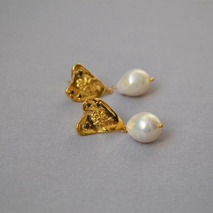 Détail de boucles d'oreilles cœur doré avec relief rose et perle baroque blanche