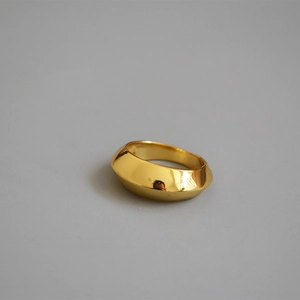 Polished gold wide-band brass ring with a geometric beveled surface on a grey background