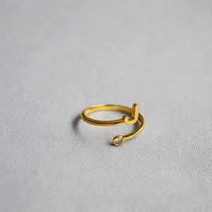 Close-up of golden adjustable ring with letter J and sparkling crystal on grey fabric
