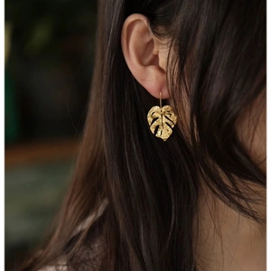 Macro detail of monstera leaf earring featuring hammered texture and golden finish on model