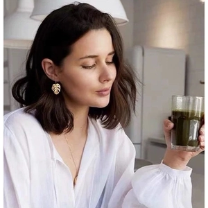 Close-up of golden monstera leaf earrings worn by a model in a modern lifestyle setting