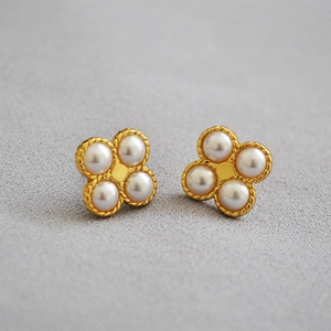 Macro shot of gold brass four-leaf clover earrings with white pearls and 925 silver studs