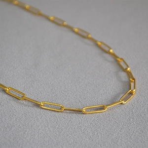 Macro detail of the gold-plated paperclip link chain with a high-polished metallic finish