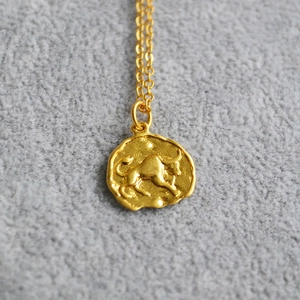 Close-up of golden Taurus zodiac coin pendant necklace on grey velvet background