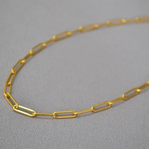 Close-up of high-gloss gold paperclip chain necklace with sleek oval links on fabric