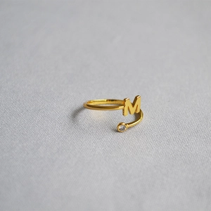 Macro shot of an adjustable gold letter M ring featuring a sparkling zircon stone