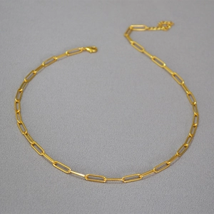 Detail view of a gold paperclip chain necklace with lobster clasp on a dark background