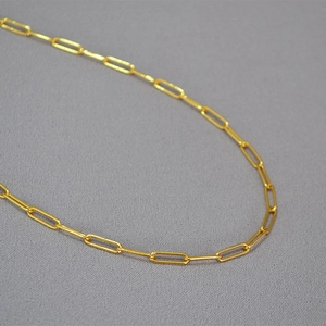Macro shot of minimalist gold paperclip chain necklace with high-polish metallic texture