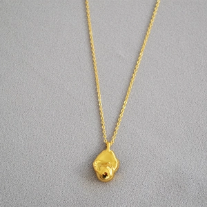 Macro view of gold-plated minimalist necklace with an irregular organic lava-style pendant