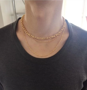 Detail of layered gold-plated brass necklace with chunky U-link and delicate bead chains