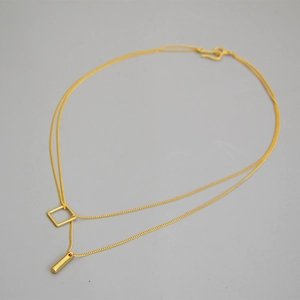 Double-layered golden necklace with geometric square and bar pendants on grey background