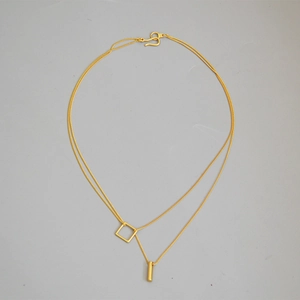 Detail of gold layered necklace with geometric square and cylinder pendants