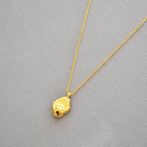 Close-up of gold-plated brass necklace with irregular lava-style pendant and polished finish