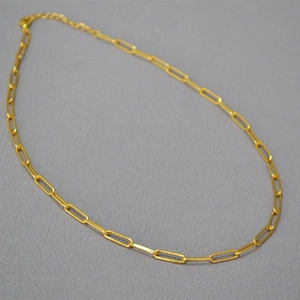 Detail of gold paperclip chain necklace with lobster clasp on grey fabric background