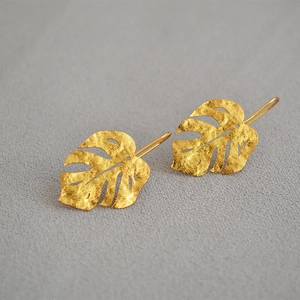 Macro detail of golden monstera leaf earrings with vintage matte granular texture finish