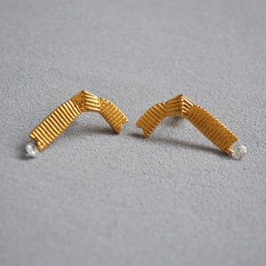 Detail view of gold ribbon stud earrings with vertical texture and small zircon stone