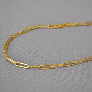 Close-up of polished gold paperclip chain link showing shiny metal texture and finish