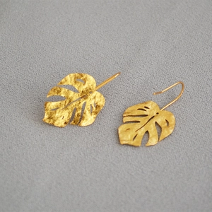 Golden monstera leaf drop earrings with textured hammered finish on grey background
