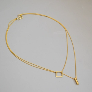 Detail of gold double-layer necklace with geometric square and cylinder pendants