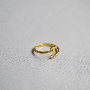Detail of gold letter T ring with a single clear zircon on a soft grey fabric surface