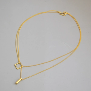 Detail of double-layer gold necklace with geometric square and bar pendants on gray base
