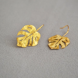 Macro view of matte gold monstera leaf earrings with intricate hollowed vein details