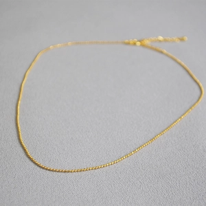 Detailed view of a minimalist gold bead chain necklace with lobster clasp and extender
