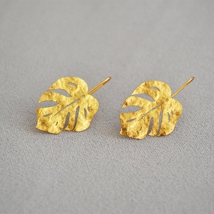 Detailed view of monstera leaf gold earrings with a matte hammered metal texture