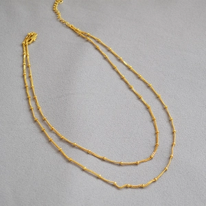 Detailed shot of double-layered 18K gold-plated beaded chain necklace on grey fabric