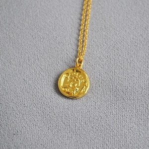 Detailed macro shot of a gold coin necklace featuring a fine portrait relief on a round charm