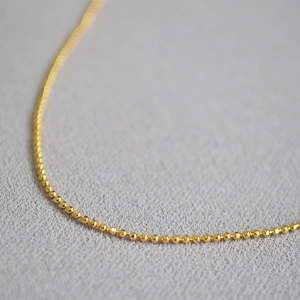 Minimalist gold beaded choker necklace with a high-polished finish on a neutral surface