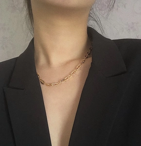 Détail d'un collier chaîne doré aux maillons texturés porté sur un costume noir