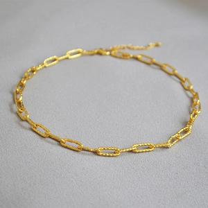 Collier à maillons trombone dorés texturés présentés sur un fond en tissu gris élégant