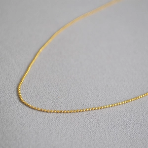 Macro detail of minimalist gold bead chain necklace on a soft grey textured fabric